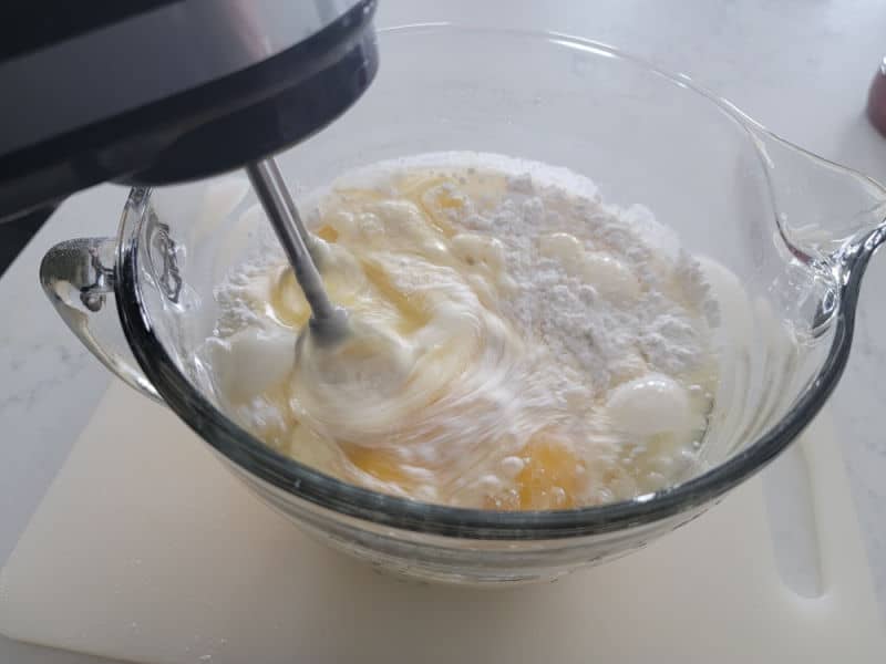 Hand mixer mixing eggnog cake ingredients in a glass bowl