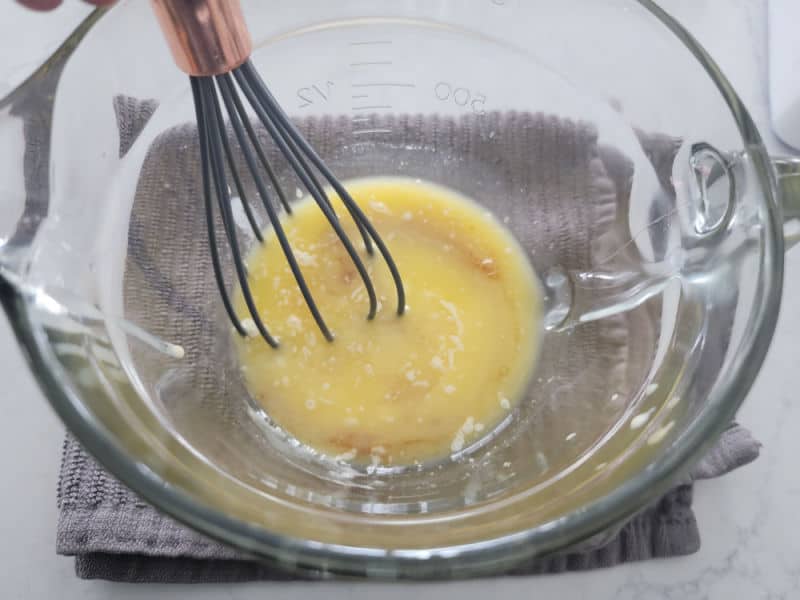 Eggnog glaze ingredients in a clear glass bowl with a whisk