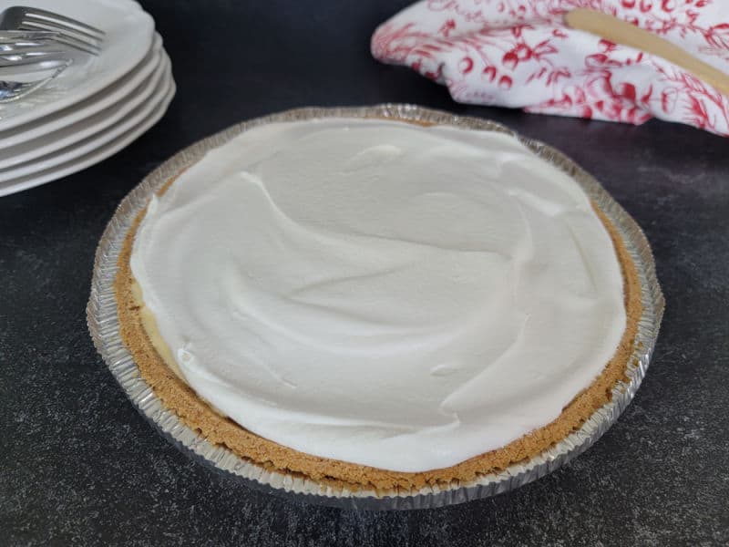 No bake eggnog pie topped with cool whip on a dark counter next to plates and forks