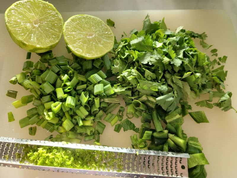 lime, chopped green onion, chopped cilantro, and lime zest on a cutting board for Cranberry Salsa