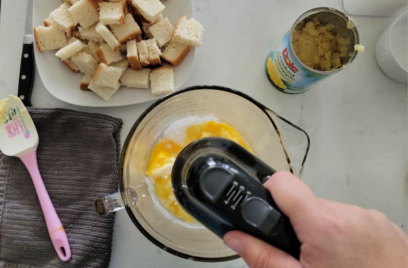 hand mixer in a bowl next to bread pieces and pineapple in a can