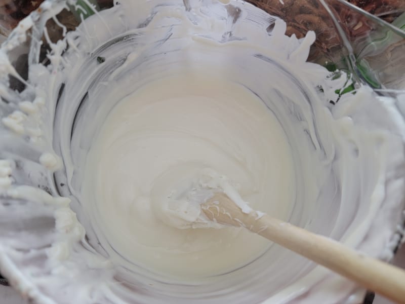 White almond bark melted in a glass bowl with a wooden spoon for Reindeer Muddy Buddies