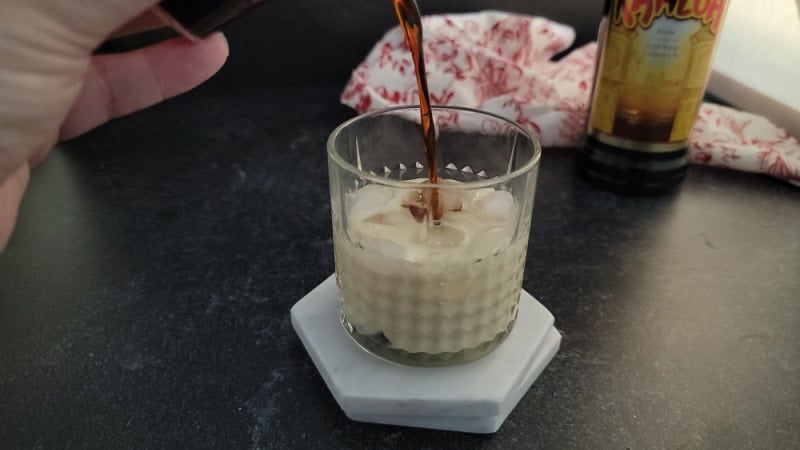 Kahlua pouring into an Eggnog White Russian Cocktail in a crystal glass