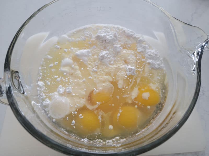 Vanilla cake mix in a glass bowl with eggs before mixing for eggnog cake