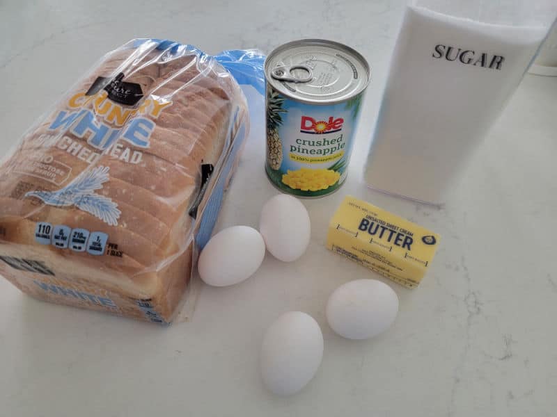 Pineapple stuffing ingredients, white bread, eggs, pineapple juice, butter, sugar on a white quartz counter