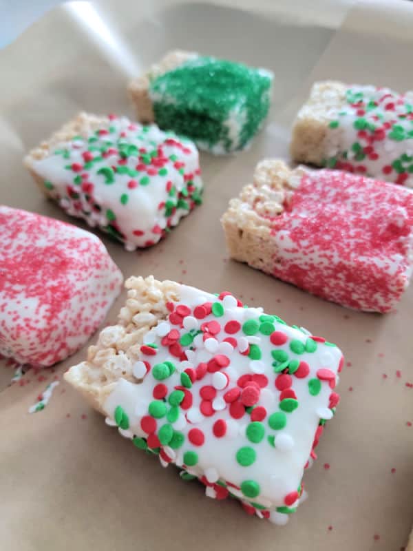 Chocolate covered rice krispie treats covered in holiday sprinkles on parchment paper