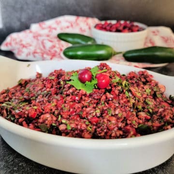 cranberry salsa in a white bowl with jalapenos and cranberries in the background