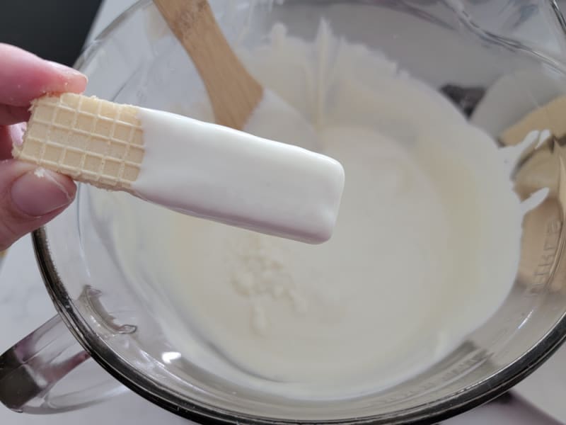 Vanilla Wafer dipped in white chocolate above a bowl of melted chocolate