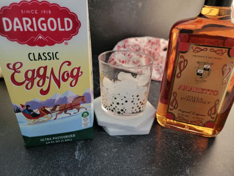 Amaretto Eggnog ingredients next to a clear glass, classic eggnog and amaretto