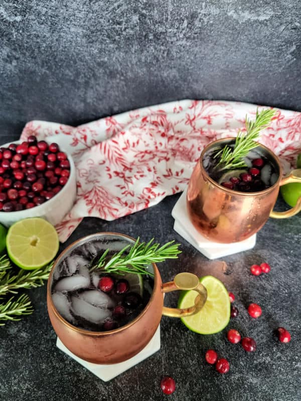 Cranberry Moscow Mule in a copper mug garnished with cranberries and rosemary next to a bowl of cranberries