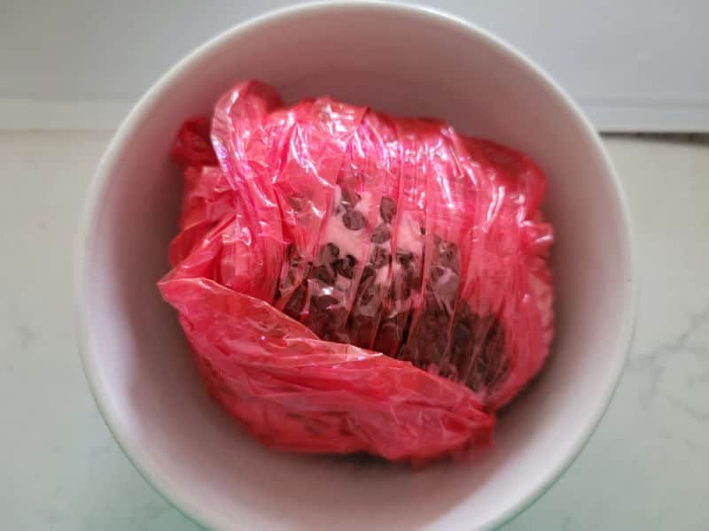 red plastic wrap around a chocolate chip cheese ball in a white bowl