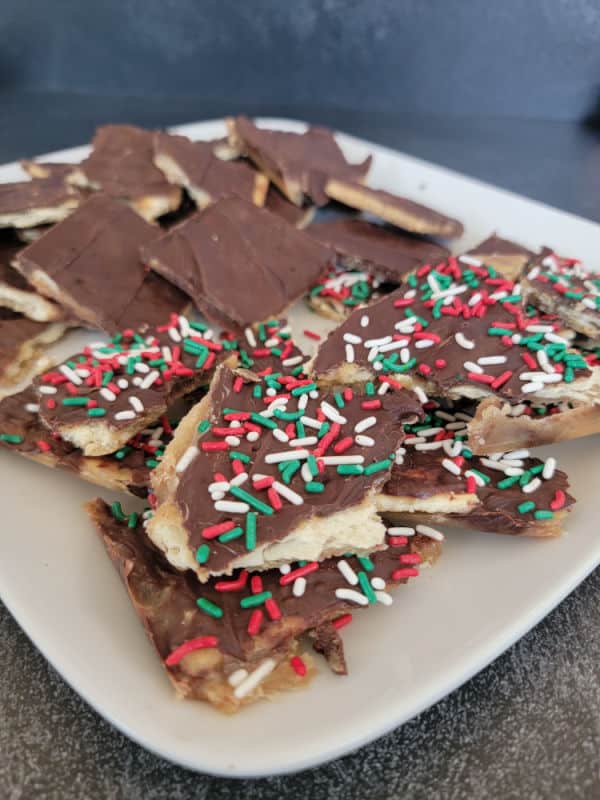 Christmas Crack Saltine Cracker Toffee on a white plate covered in holiday sprinkles
