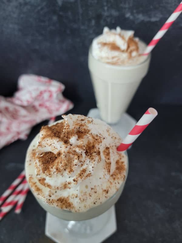 Eggnog shake in a milkshake glass garnished with whipped cream and ground nutmeg with a red striped staw