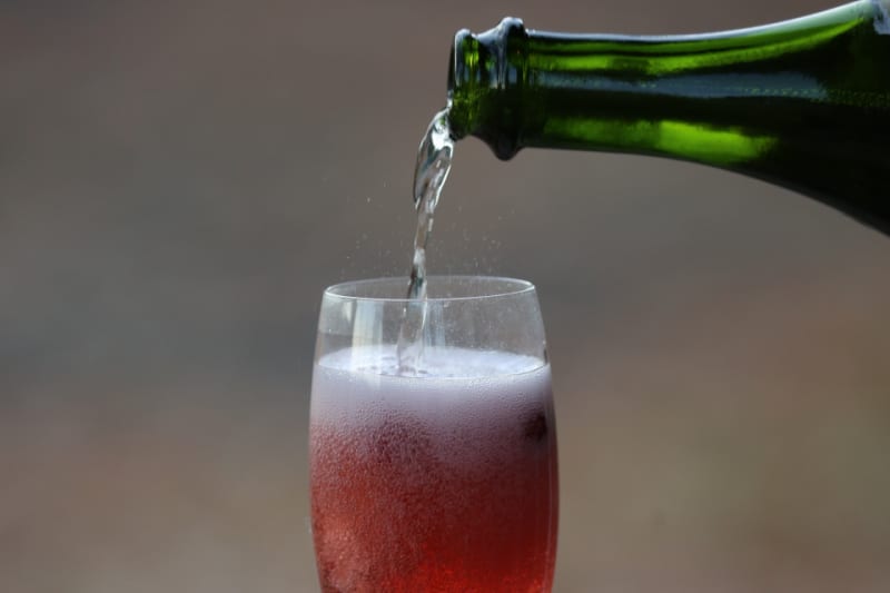 Champagne pouring into a cranberry mimosa in a champagne flute