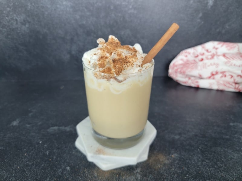 Clear glass with an Eggnog Mudslide topped with whipped cream, ground cinnamon and nutmeg, with a cinnamon stick