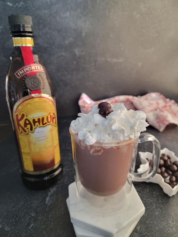 Kahlua Hot Chocolate with whipped cream in a glass mug next to a bottle of Kahlua