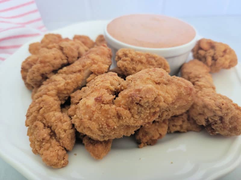 Chicken strips on a white plate next to a bowl of sauce