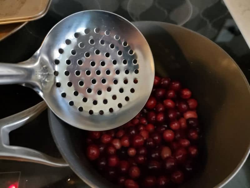 slotted spoon going into a sauce pan filled with sugared cranberries