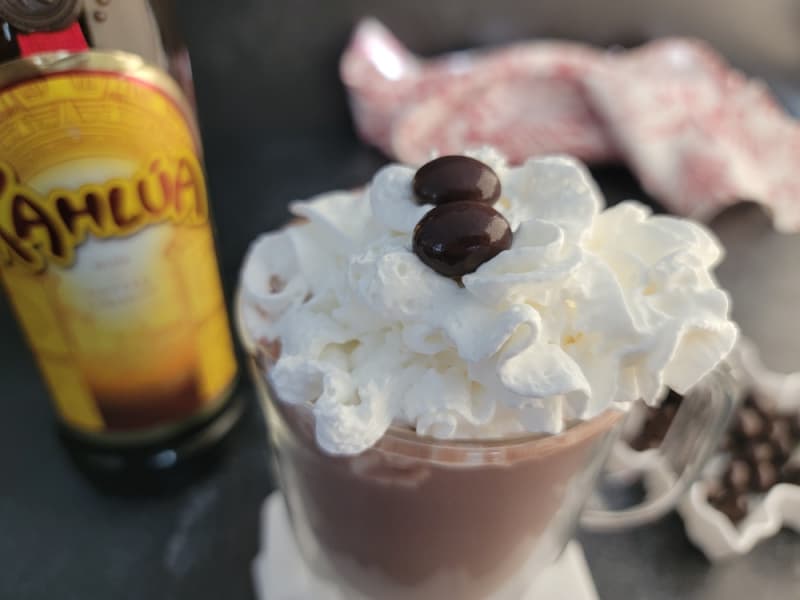 Kahlua Hot Chocolate with whipped cream in a glass mug next to a bottle of Kahlua