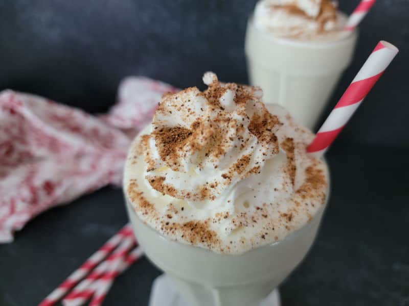 Eggnog milkshake garnished with whipped cream and ground nutmeg with a red strip straw in a glass