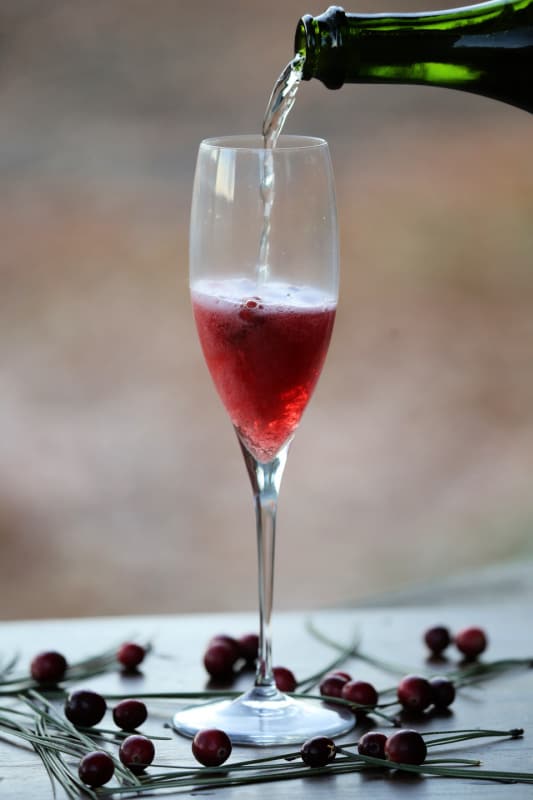 Champagne pouring into a champagne glass with cranberries in it