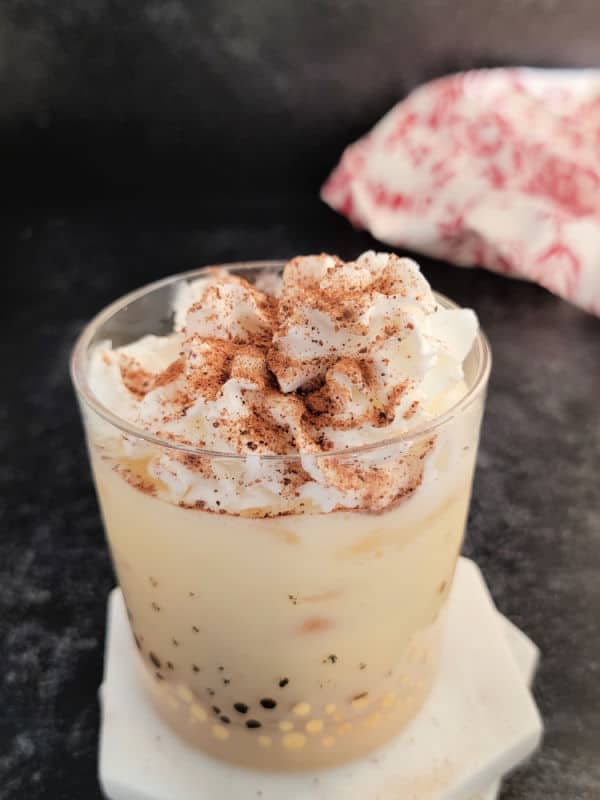 Eggnog drink in a glass with whipped cream and nutmeg garnish. Cloth napkin in the background