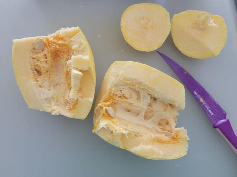 cut spaghetti squash next to a purple knife on a cutting board. 