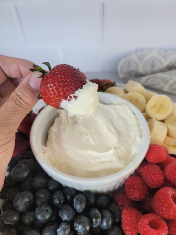 Strawberry dipping into a white bowl with marshmallow fluff fruit dip surrounded by fresh fruit