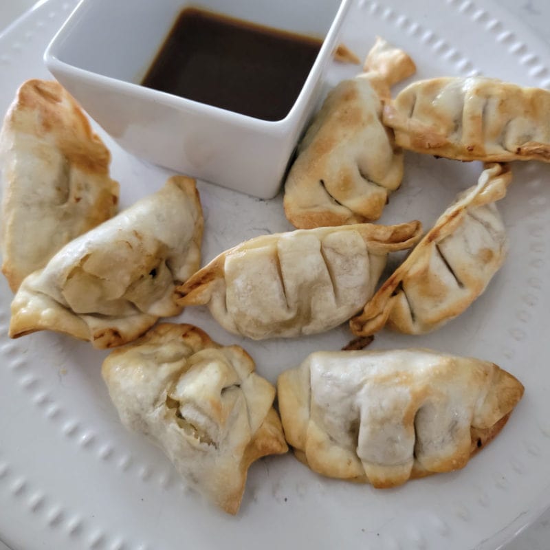 Air fried dumplings on a white plate with dipping sauce