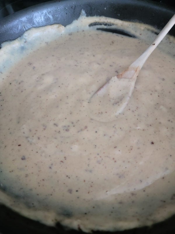 wooden spoon resting in bacon gravy in a dark skillet