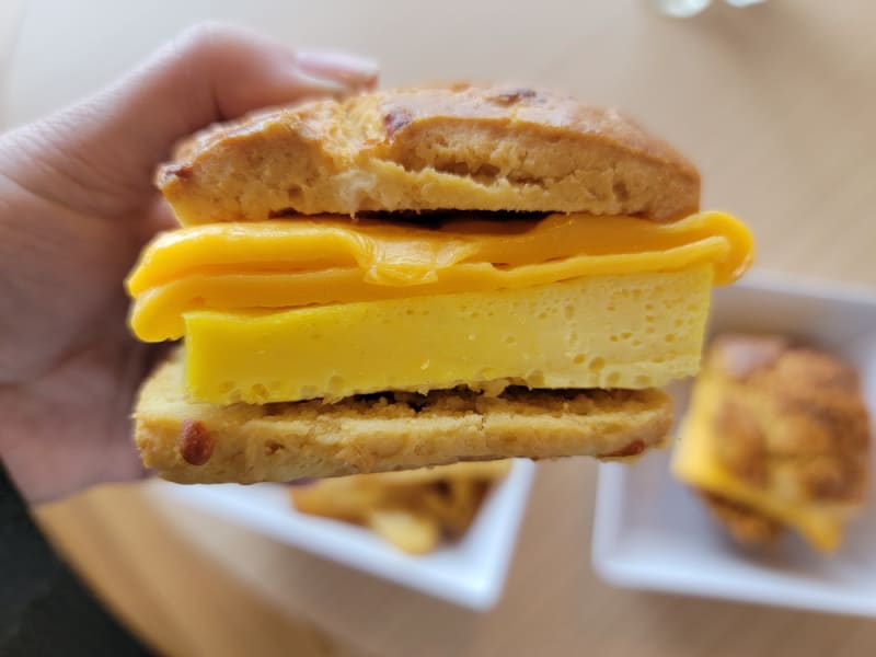 Hand holding a biscuit with cheese and egg over two plates