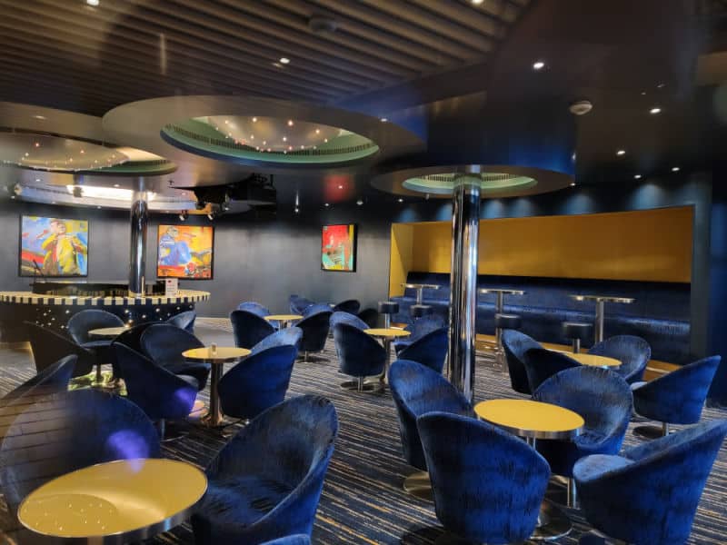 blue velvet chairs next to yellow topped tables in a lounge area 