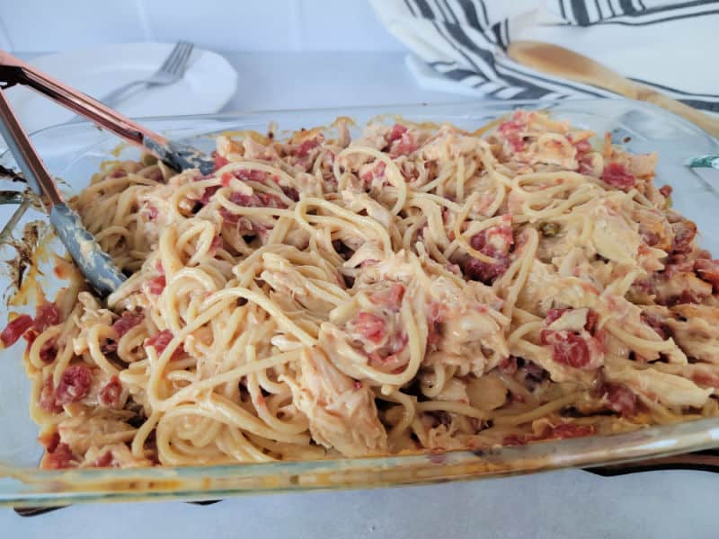 Chicken Spaghetti Rotel in a glass casserole dish with tongs for serving