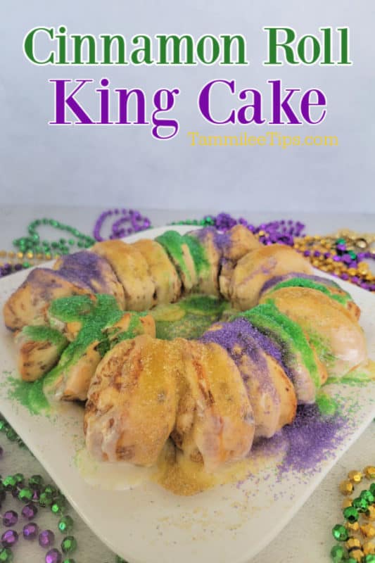 Cinnamon Roll King Cake over a white platter with cinnamon rolls, purple, gold and green sprinkles surrounded by mardi gras beads