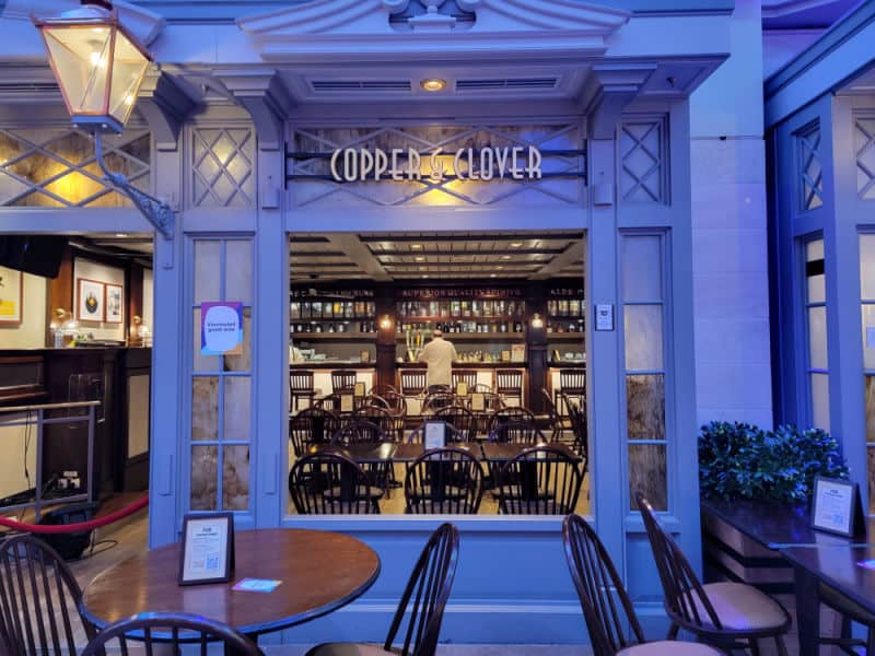 Cooper & Clover bar entrance with a bartender, tables and chairs through an open window. 