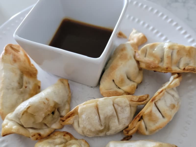 air fryer dumplings on a white plate next to dipping sauce