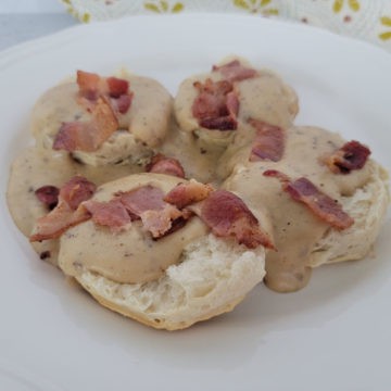 Bacon gravy over biscuits on a white plate with a cloth napkin in the background