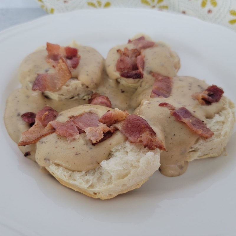 Bacon gravy over biscuits on a white plate with a cloth napkin in the background