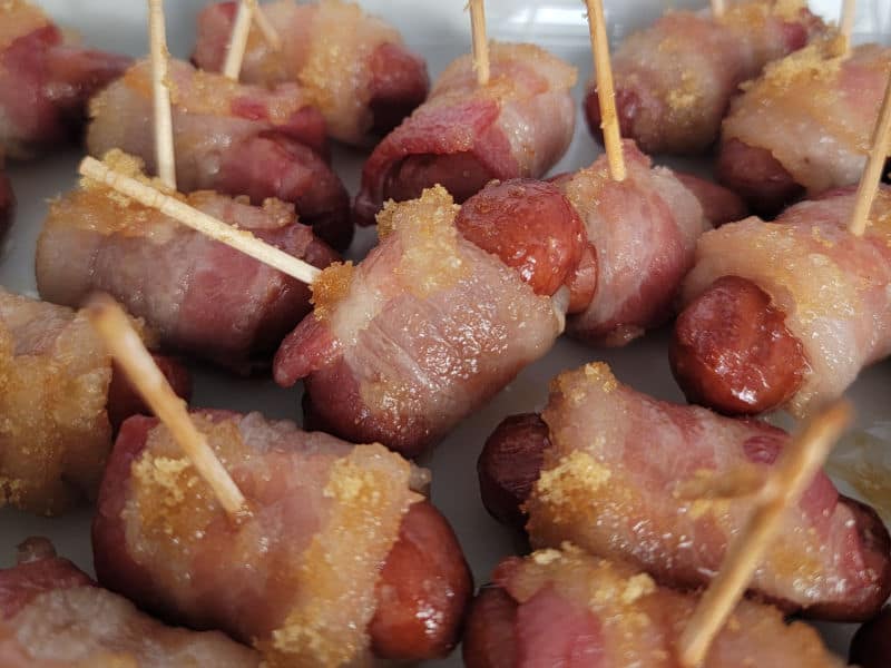 Baked with Brown sugar bacon wrapped little smokies with toothpicks on a white platter