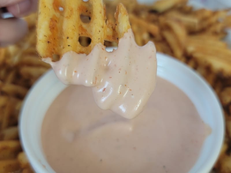 Waffle fry dipping into Fry Sauce in a white bowl. 