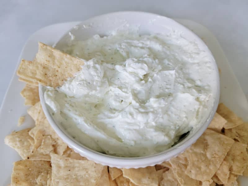 Ranch dip in a white bowl surrounded by tortilla chips on a white platter
