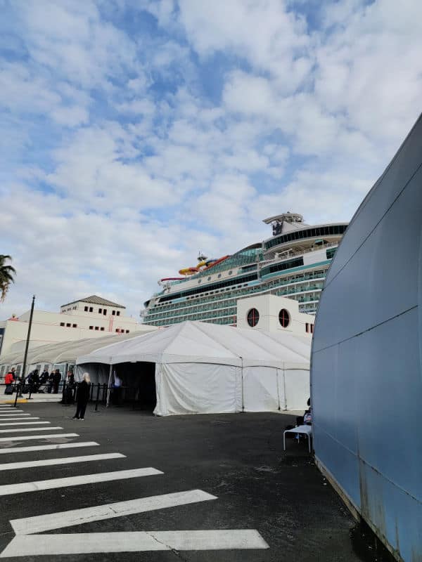 White tents with people on the dock with the top of a cruise ship behind them. 