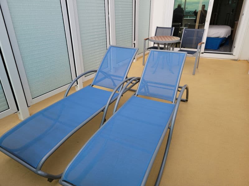 Two lounge chairs on a deck with a stateroom entrance door in the background. 