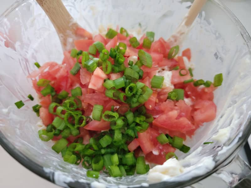 Diced tomatoes and green onions in a glass bowl with a wooden spoon 