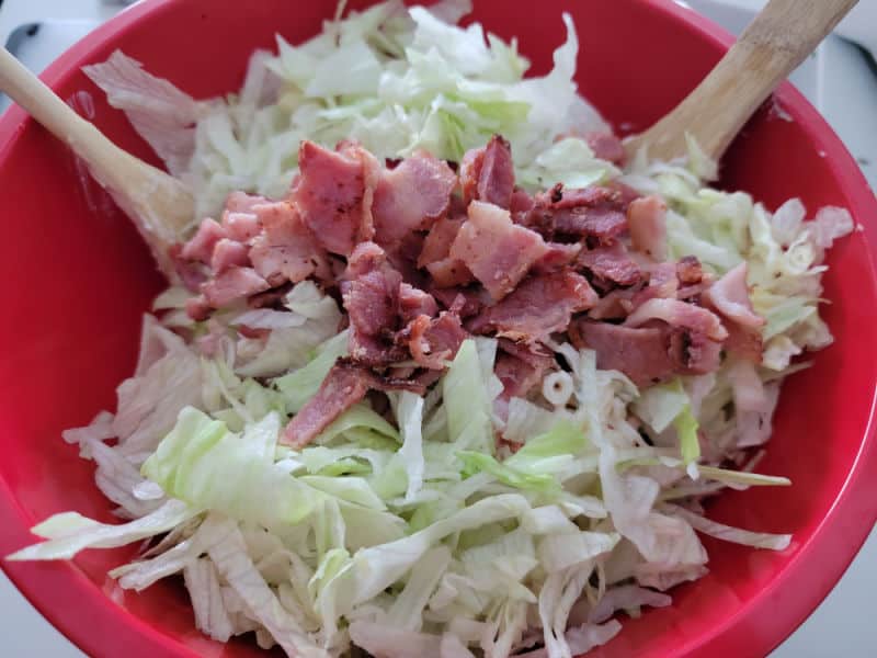 Bacon pieces and lettuce in a red bowl with wooden spoons