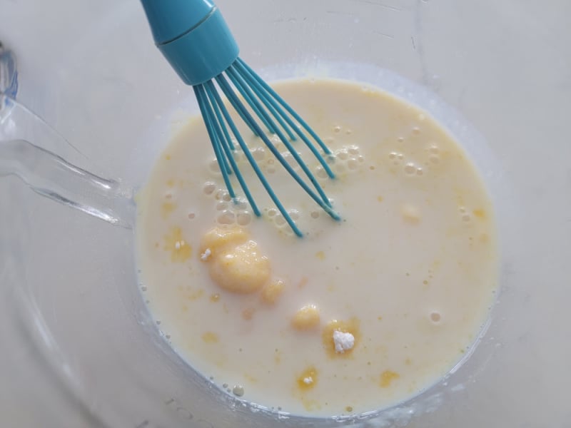 Vanilla pudding mix in a clear glass bowl with a blue whisk for RumChata Pudding Shots