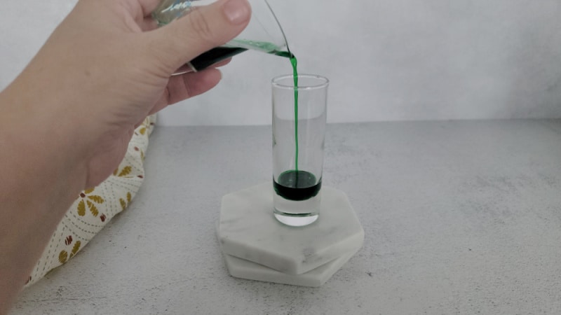 green liquid pouring into a glass shot glass on a white coaster