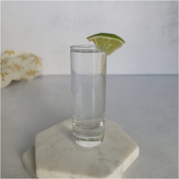 Kamikaze shot in a glass shot glass with lime wedge on white coasters