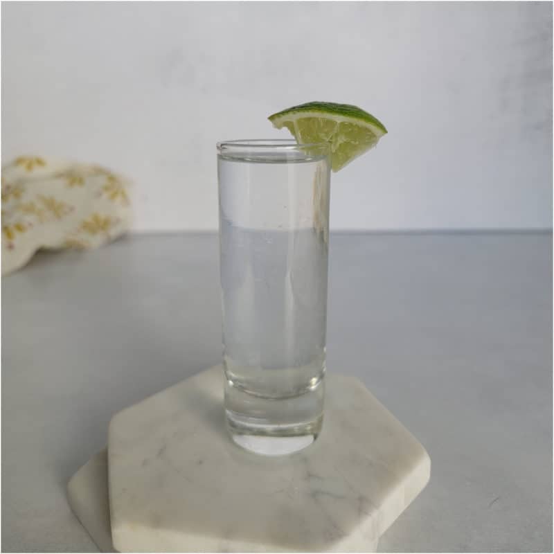 Kamikaze shot in a glass shot glass with lime wedge on white coasters