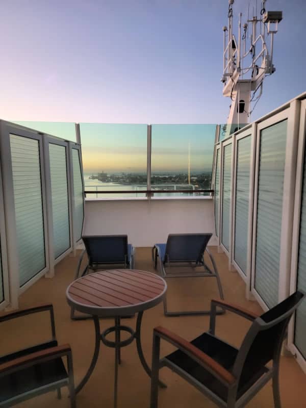 table and chairs near lounge chairs with the ocean and a city in the background